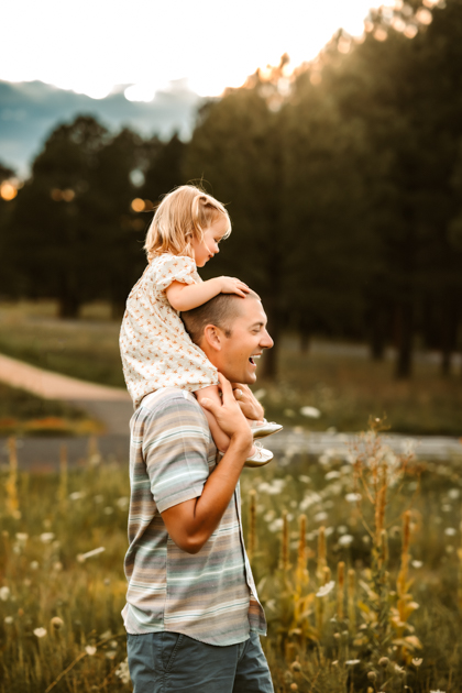 Daughter on dad's shoulders laughing in a field of wildflowers at Forest Highlands Golf Club in Flagstaff.