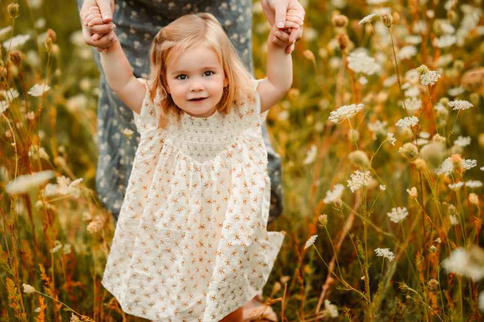 Mom holding toddler daughter's hands as she smiles for a portrait in a field of wildflowers in Flagstaff, Arizona.