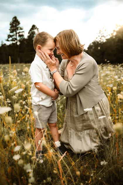 Grandmother and grandson kissing in a field of wildflowers during summer monsoons in Flagstaff, Arizona portrait session.