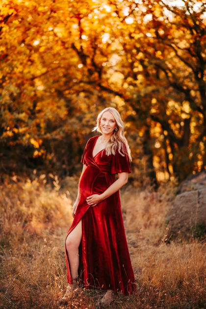 Pregnant woman in a red velvet gown posing for a maternity session at Buffalo park in Flagstaff, AZ.