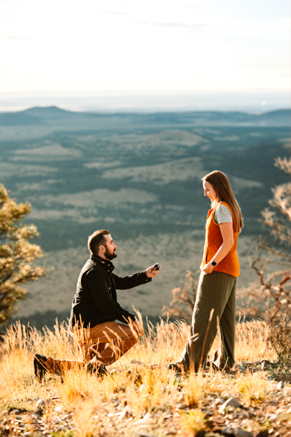 Man proposing on one knee at the top of Slate Mountain in Flagstaff, Arizona by Annie Bee photography.