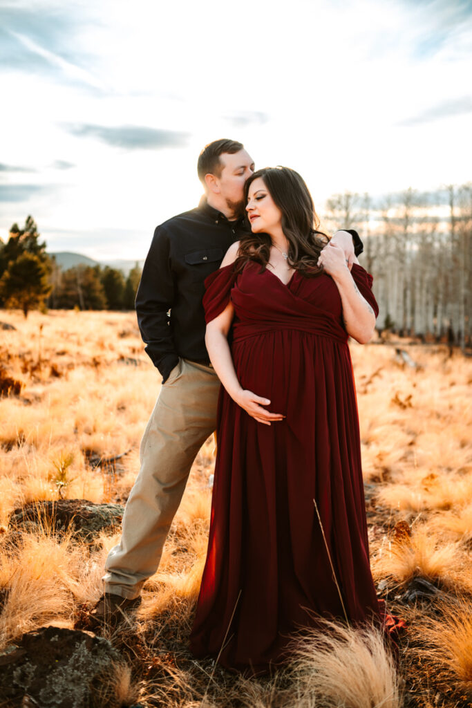 Maternity photos at Arizona Snowbowl of women in a red dress and husband holding her.