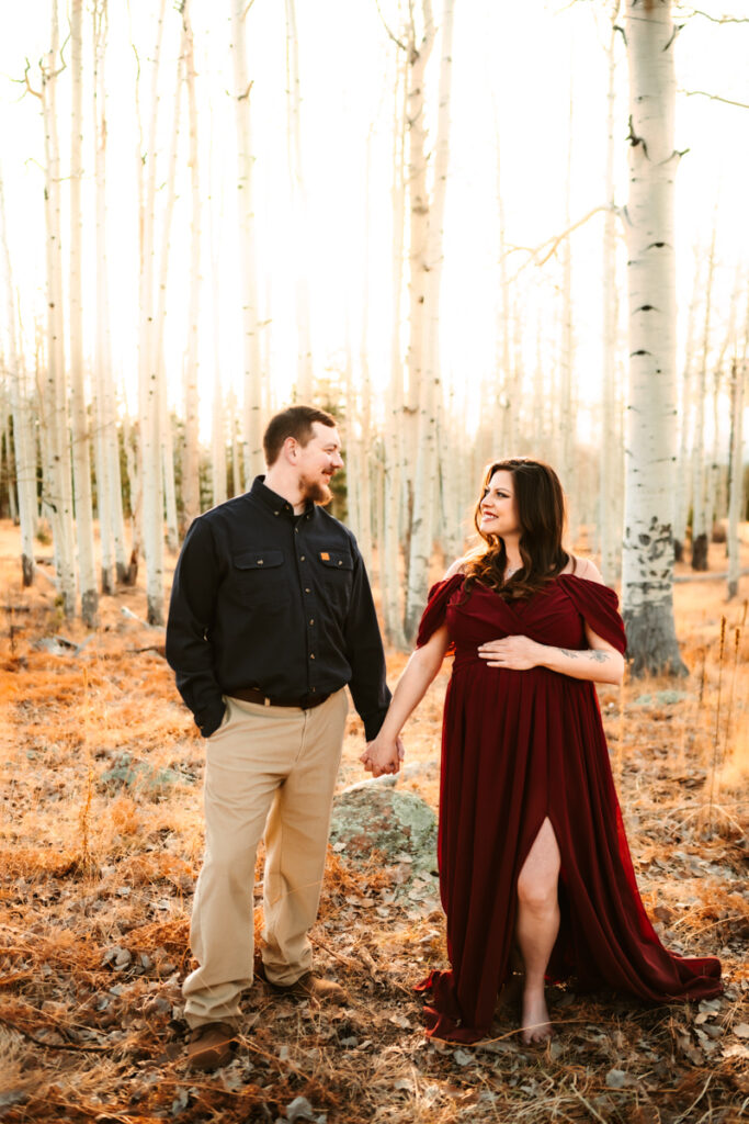 Husband and wife holding hands in the aspen trees at Aspen Corner during maternity photos.