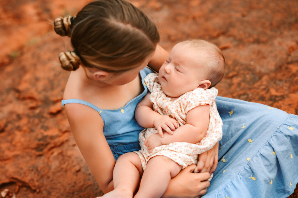 Sister holding baby sister while she is sleeping in the red rocks of Sedona.