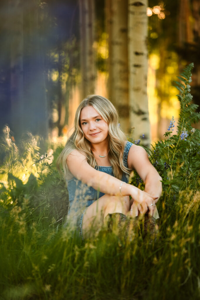 Senior graduate posing in the purple wildflowers wearing a jean dress on Snowbowl.