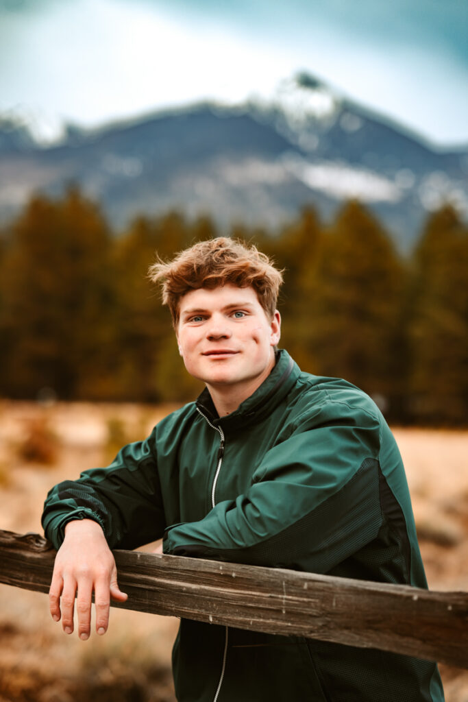 Senior boy in front of Arizona snowbowl leaning on a fence by annie bee photography.