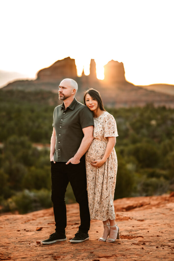 Women expecting a baby holding her belly with her husband in the red rocks of sedona.
