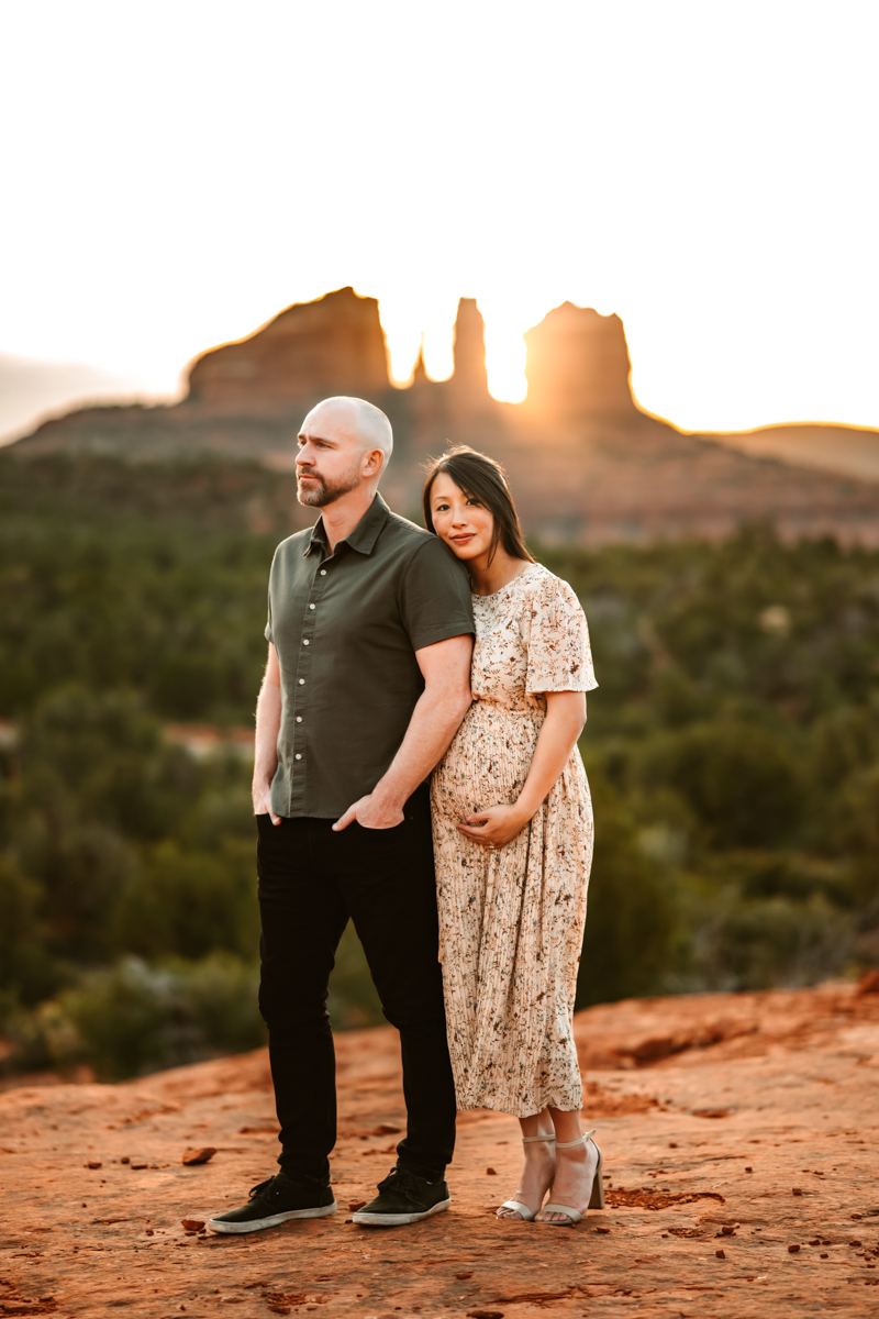 Women expecting a baby holding her belly with her husband in the red rocks of sedona.