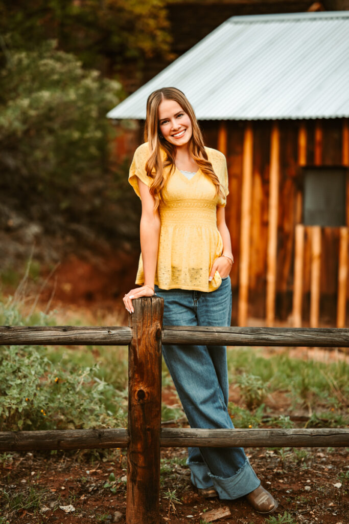 Senior girl leaning on a fence in front of a barn in sedona by annie bee photography.