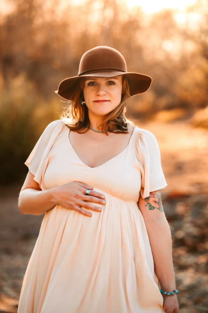 Expecting mom at a maternity session holding her belly with a brimmed hat at Red Rock Crossing.