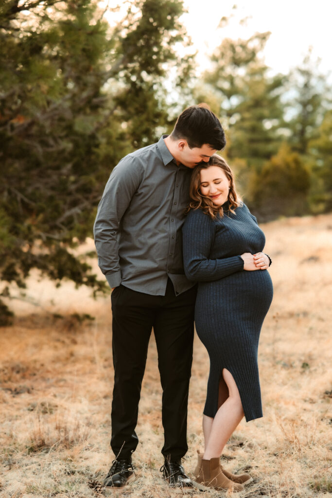 Husband and wife expecting a baby cuddling in the forest at the best Flagstaff photo locations.