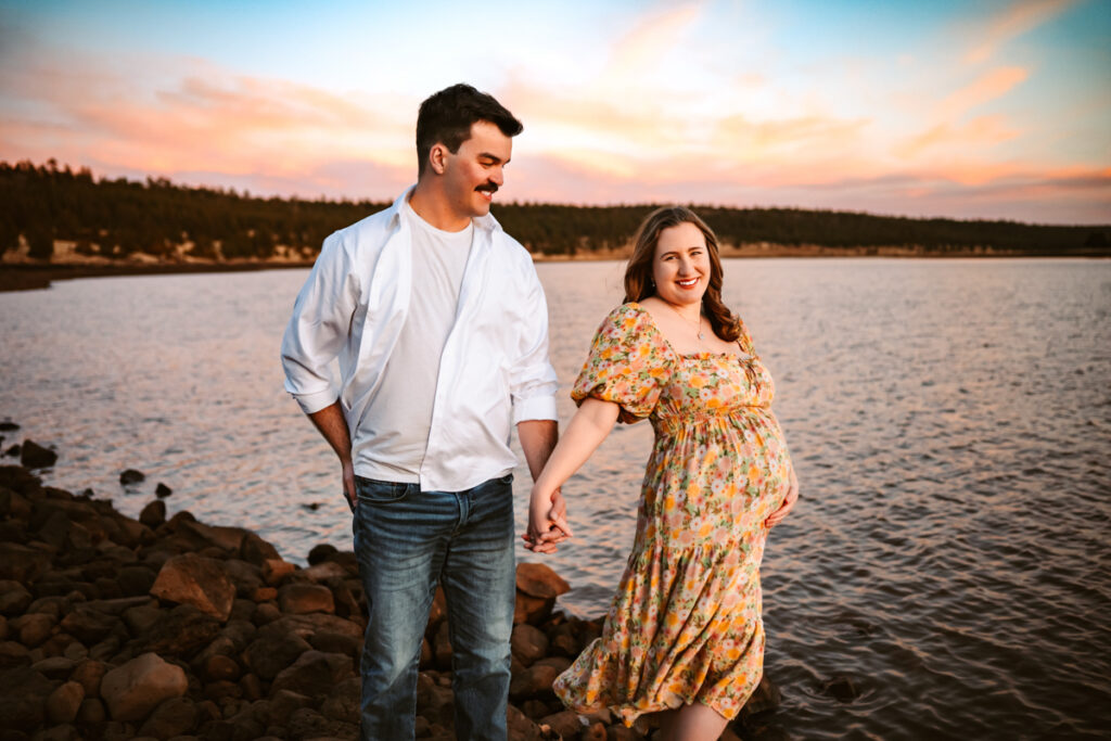 Expecting couple holding hands in front of a lake in flagstaff.