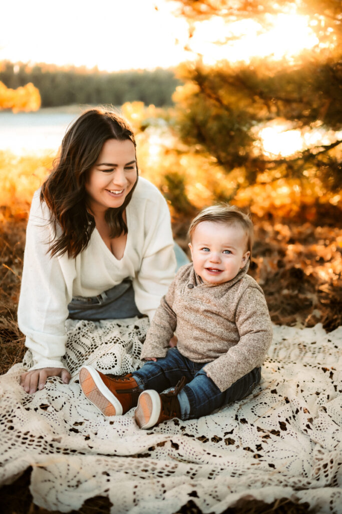 Mother laughing at her toddler who is sitting on a blanket in front of lake mary in flagstaff.