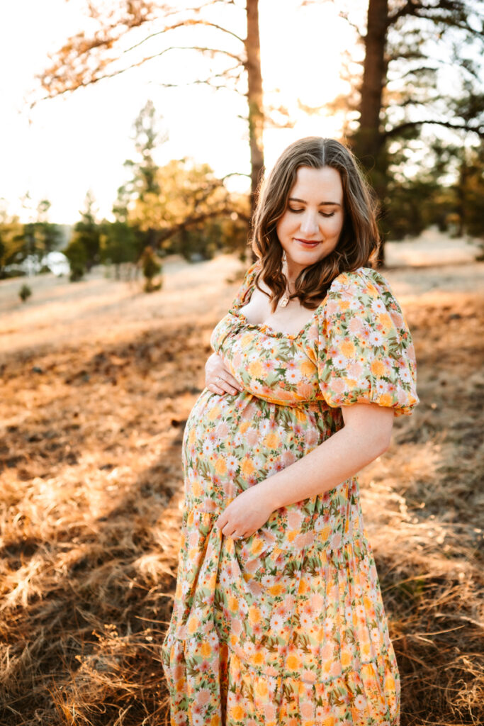 Expecting mom in a maxi dress holding her belly in the forest of Flagstaff.