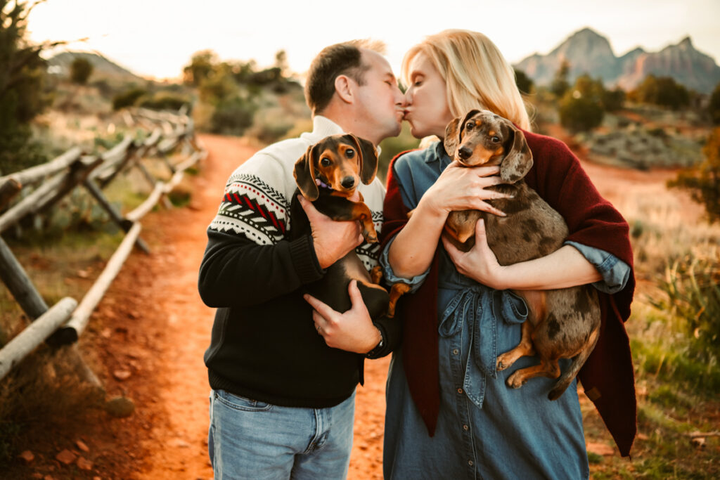 Parents kissing holding their dogs in the red rocks of sedona.