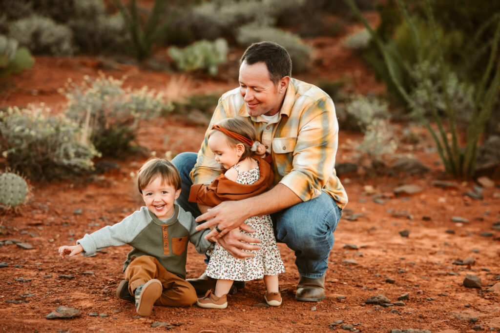 Dad holding son and daughter as they play in the red rocks of sedona.