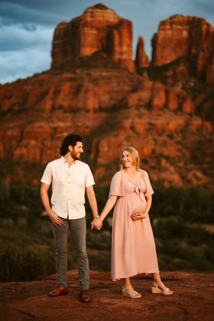 Pregnant couple holding hands with Cathedral Rock in Sedona.